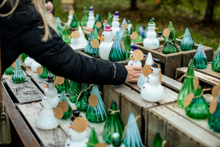 Hand reaching out for glass snow person on display with many other hand blow holiday glass projects