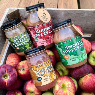 Canned jars of applesauce sitting in a bushel of Glass Orchard apples