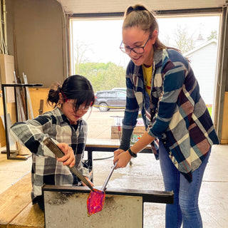 Instructor helping a young student manipulate her molten glass project