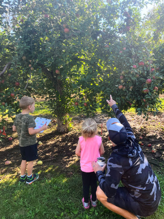 Man pointing up at a glass acorn hanging in a apple tree while children search for it