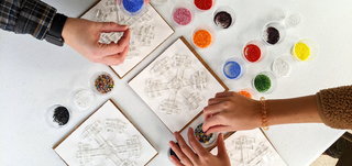 Two people making fused glass art snow flakes. 