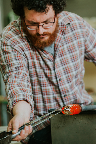 Glass artist working with equipment to form glass art 